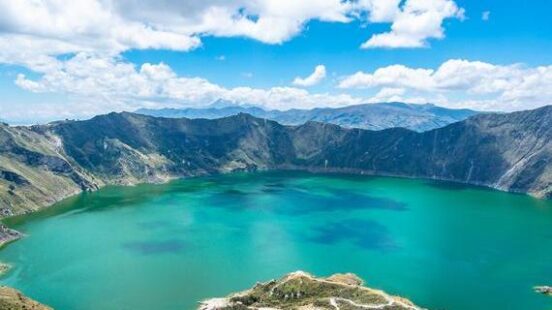 Overlook of a vibrant turquoise crater lake surrounded by steep mountain ridges.