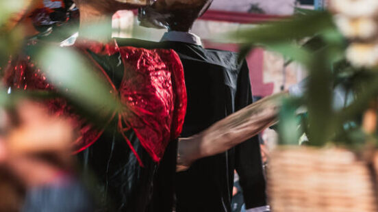 Large skull puppets in red and black clothing are featured in a festive outdoor gathering.