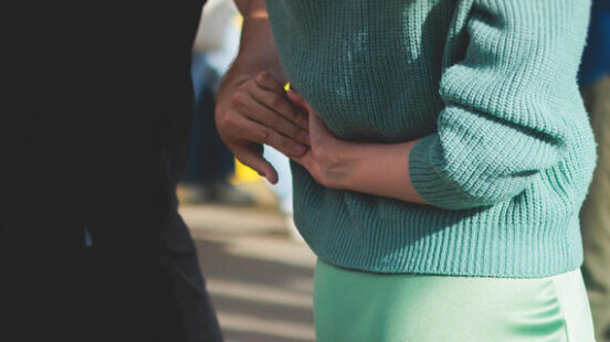 Close-up of a person in a green sweater and satin skirt dancing with a partner in a black shirt.