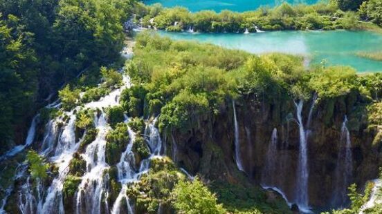 Aerial view of tiered waterfalls flowing into bright blue lakes surrounded by thick green forest.