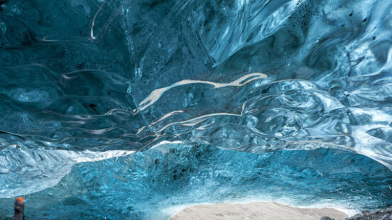 A person inside a glowing blue ice cave with swirling textures on the ceiling and a stream on the ground.