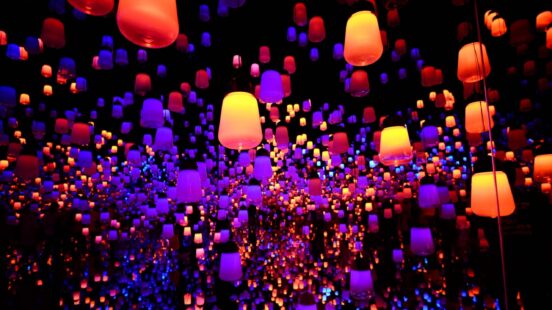 Numerous glowing purple and orange lanterns hanging at different heights in a dark room.
