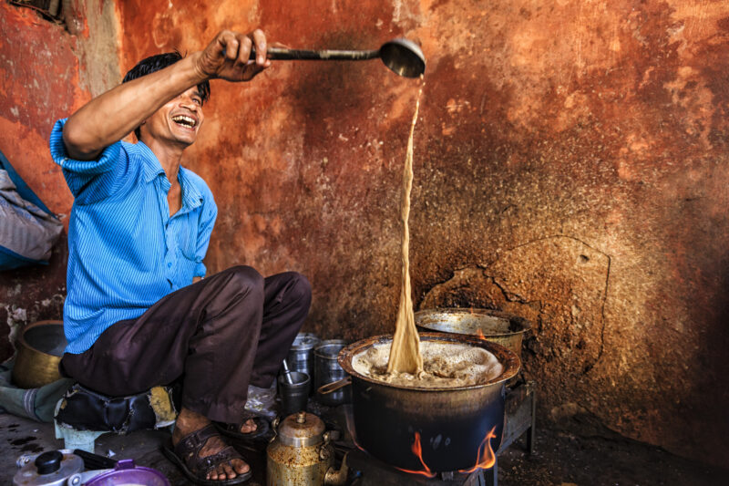 A local vendor pours hot masala chai into a pot at a traditional tea stall in India.