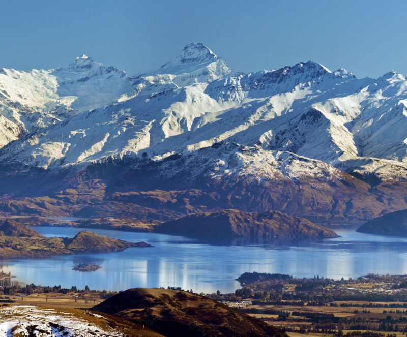 “Landscape with snowy Mount Aspiring mountain range, blue Lake Wanaka and Wanaka township. Clear blue sky.”
