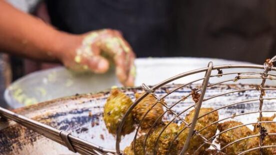 Crispy falafel balls being scooped out of bubbling deep-fry oil with a metal mesh strainer.