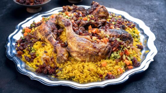 Roasted chicken pieces served on spiced yellow rice with dried fruit and nuts on a decorative silver plate.