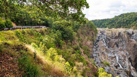 The Kuranda Scenic Railway winds through dense rainforest past a steep gorge, Queensland, Australia.