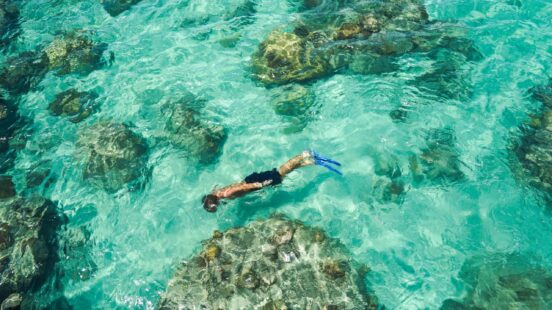 A snorkeller swims through clear, shallow waters above coral bommies – Great Barrier Reef, Australia.
