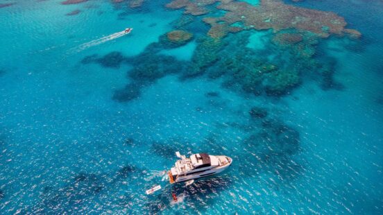 Aerial view of a private yacht anchored near vibrant coral formations – Great Barrier Reef, Australia.
