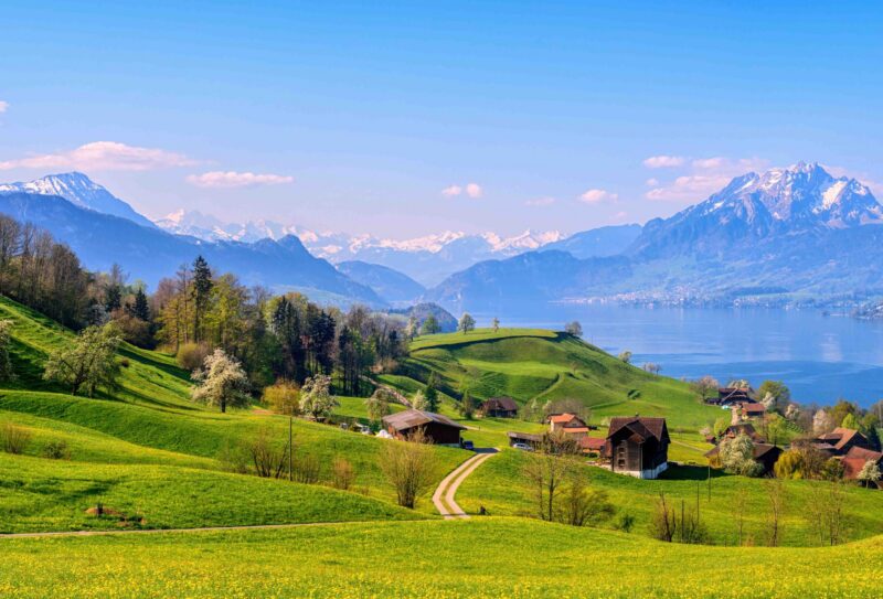 Panoramic view of Lake Lucerne, green alpine meadows blooming in spring time and the Alps mountains range with Mount Pilatus, Switzerland