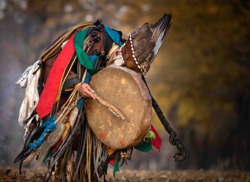 A person in a ritual costume holding a large drum, captured during luxury Mongolia vacations.