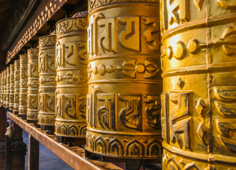 Ornate brass Buddhist prayer wheels lined up, carved with ancient mantras that catch the light.