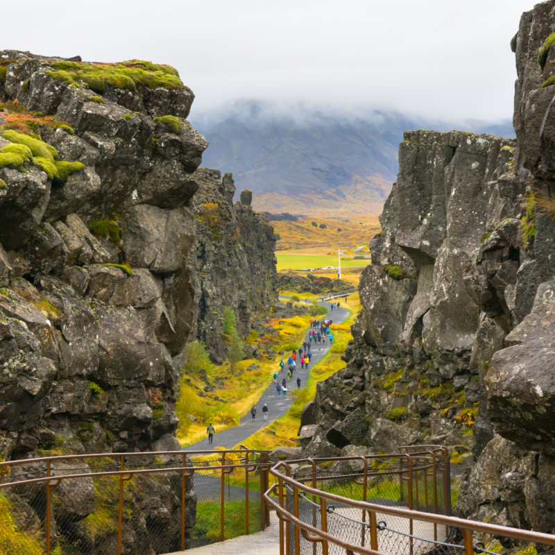 A group of people walking on a paved trail between towering rock formations under a cloudy sky during luxury Golden Circle tours.