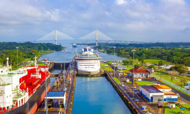 High angle view of a cruise ship and cargo ship navigating through a canal lock system near a large bridge.