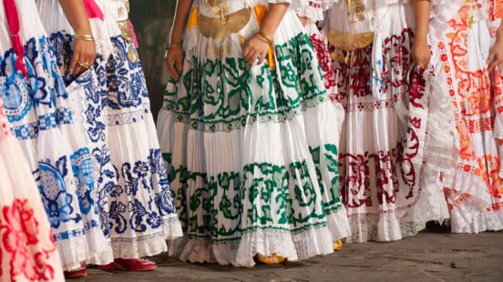 Close-up of several traditional white skirts with colorful floral embroidery and gold decorative accessories.