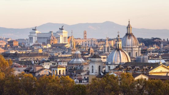 Panoramic view of the Rome skyline with historic stone buildings and large church domes.