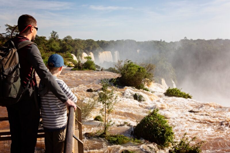 family of two, father and son, enjoying the gorgeous view of iguazu falls in argentina and brazil, adventure vacation concept