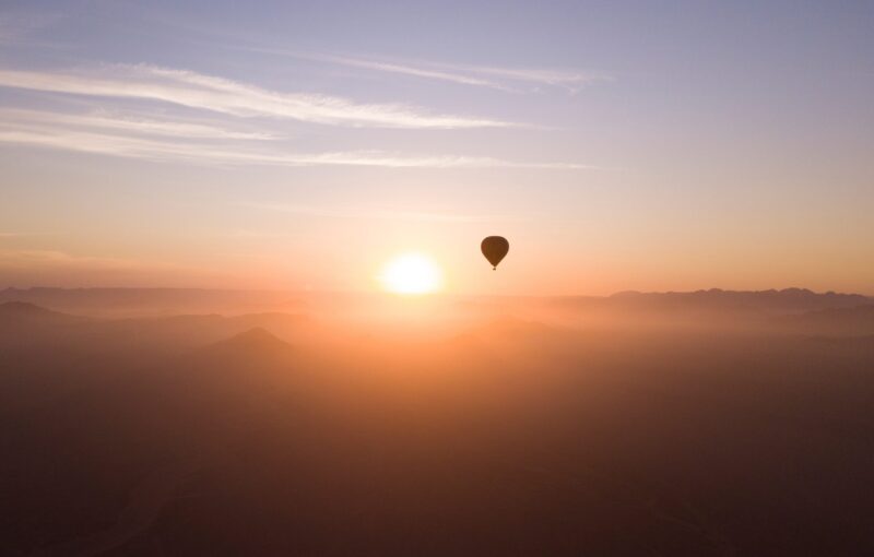 Silhouette of a hot air balloon in a bright orange sunrise sky over misty mountains.