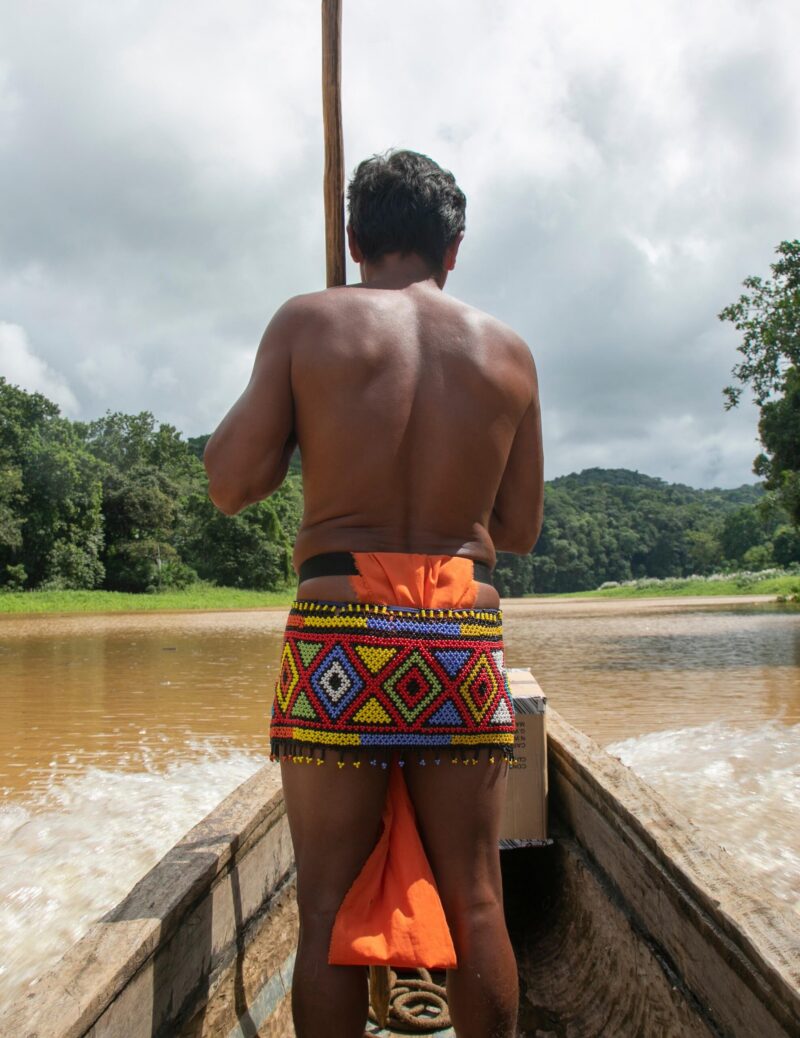 An Emberá man navigating a wooden dugout canoe down a river in the Chagres rainforest, Panama.