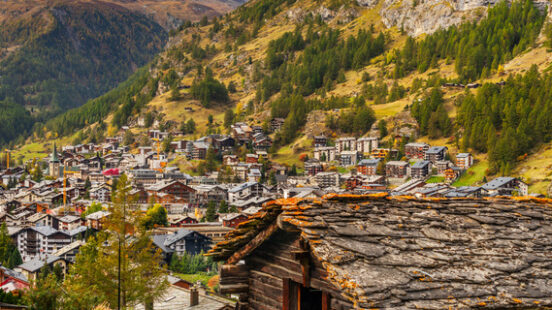 An old wooden chalet in the foreground of Zermatt village with the iconic snow-capped Matterhorn peak rising behind it.