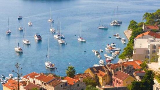 High angle view of a seaside town with terracotta roofs and numerous boats moored in a calm blue harbor.