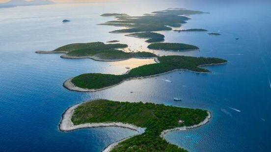 Aerial view of a series of small, forested green islands surrounded by calm blue ocean water at sunset.