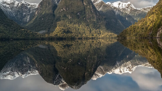 A yellow kayak glides across mirror-still waters in Milford Sound