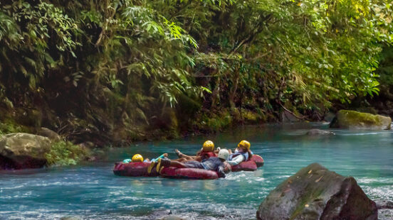 Inner tubers float down a turquoise river – framed by Costa Ricax27;s rainforest canopy.