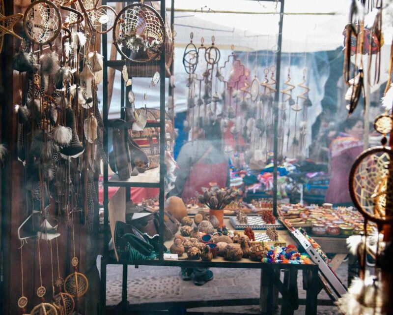 A market stall filled with hanging dreamcatchers, feathers, and various wooden handicrafts at an outdoor bazaar.