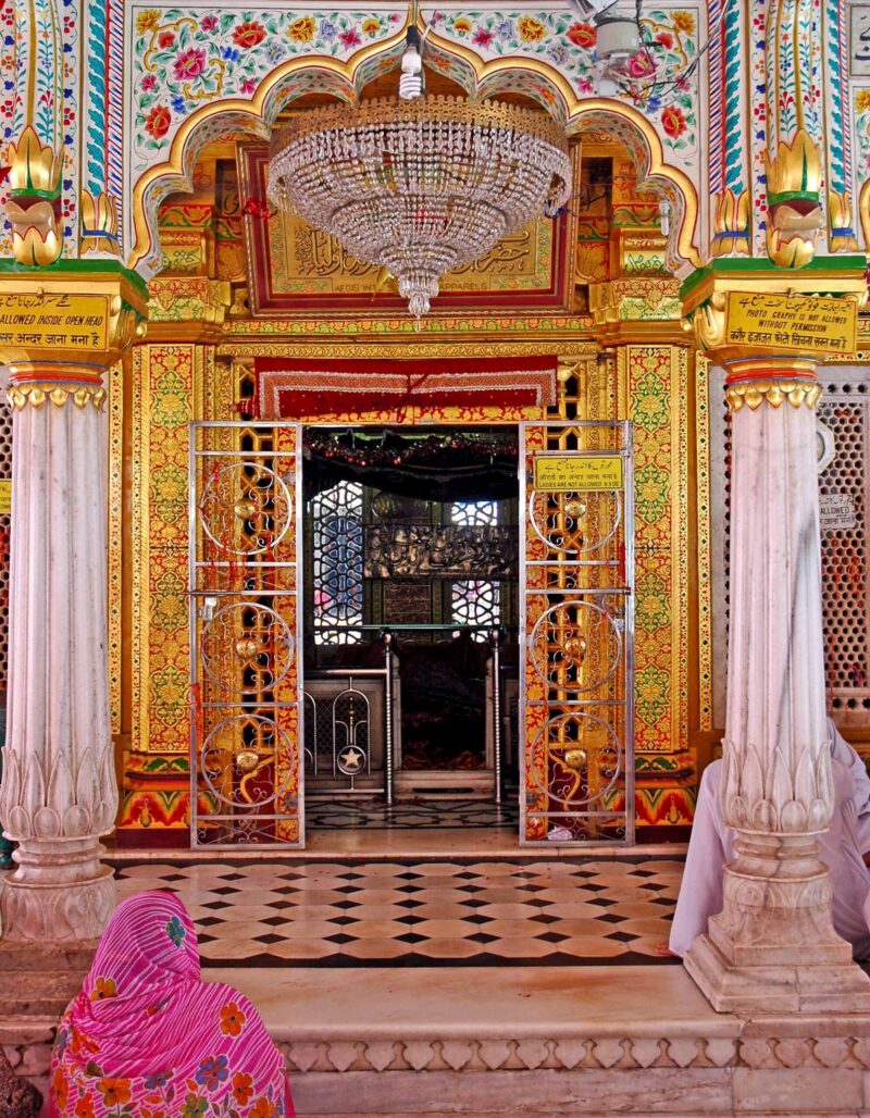 Intricate gold detail frames the sanctuary of Nizamuddin Dargah in Delhi as a devotee sits in quiet reflection.