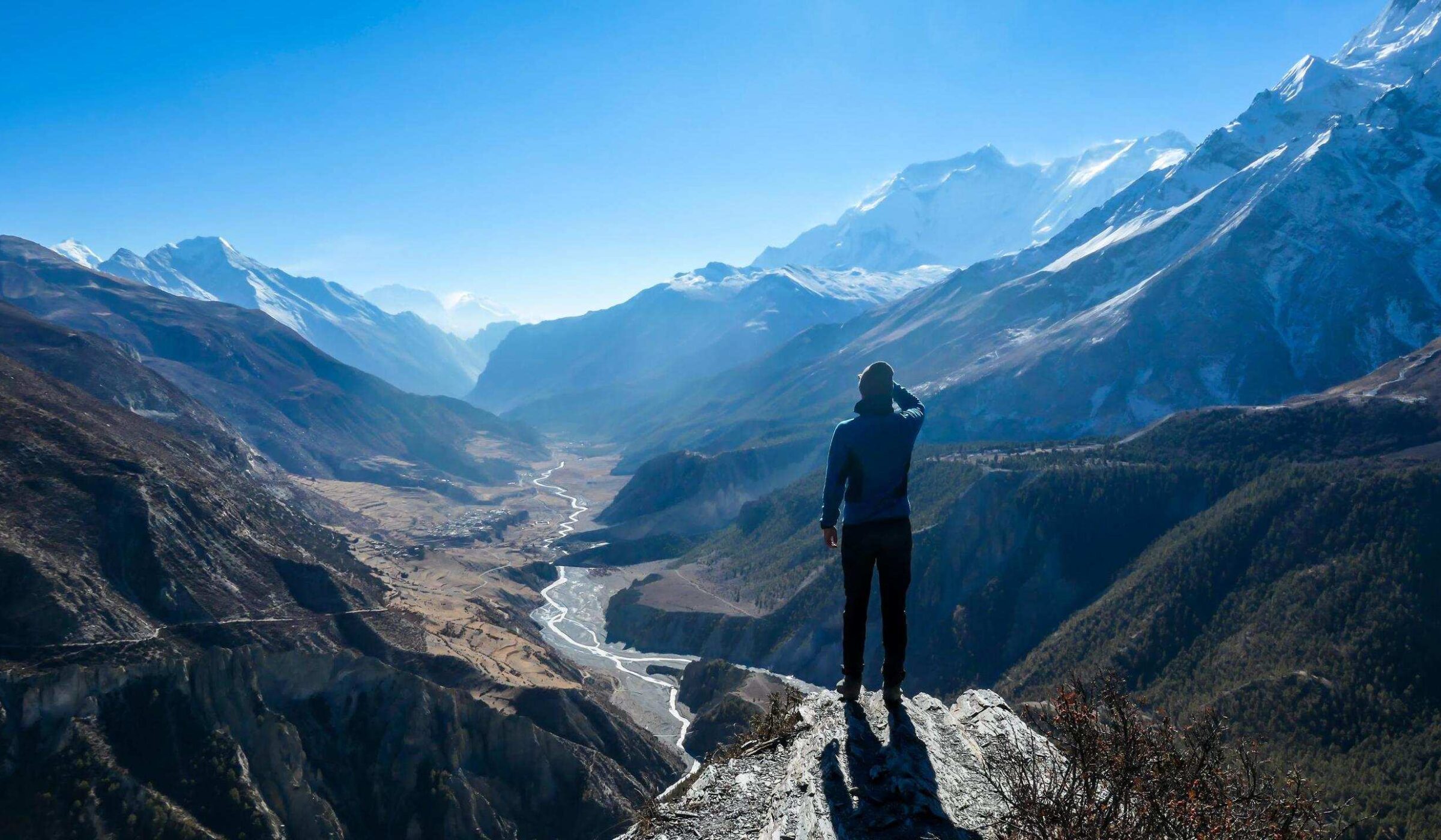 A man wearing a beanie and blue jumper, stands at the rock edge, breathing deeply the fresh mountain air. Freedom and happiness. Below Manang valley stretches in Himalayas, along Annapurna Circuit.