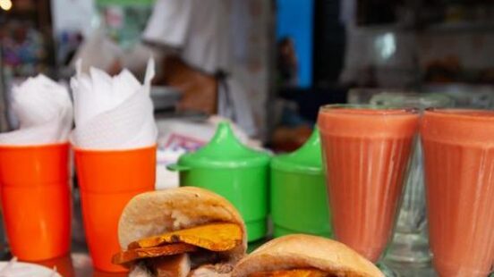 Peruvian pork sandwich on a colourful plate with glasses of orange-coloured juice and a man working in the background