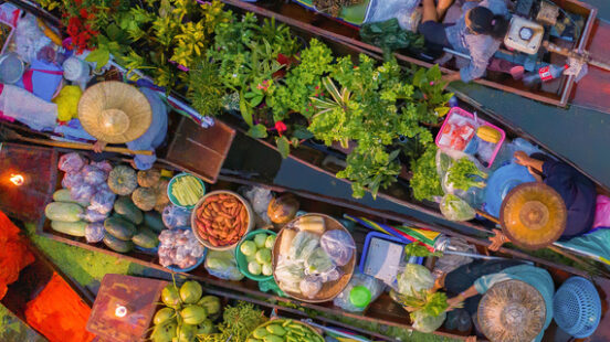 Overhead view of several long wooden boats filled with colorful produce and plants at a floating market.
