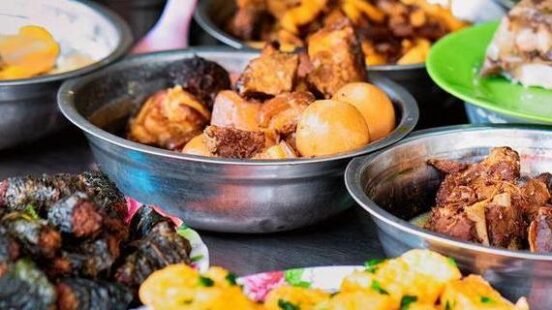Various bowls of cooked meat, eggs, and vegetables arranged on a counter at a local food stall.