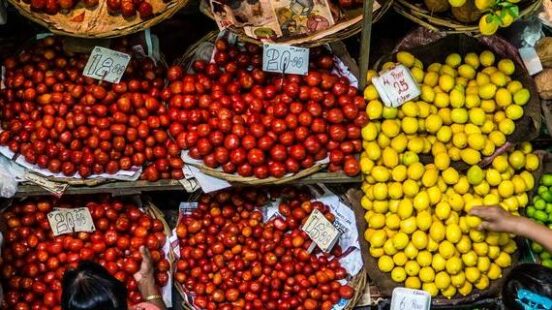 Overhead view of an outdoor market with baskets of red tomatoes, yellow lemons, orange carrots, and green limes.