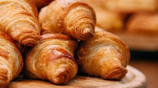 A pile of fresh, golden-brown flaky croissants stacked on a circular wooden serving board.