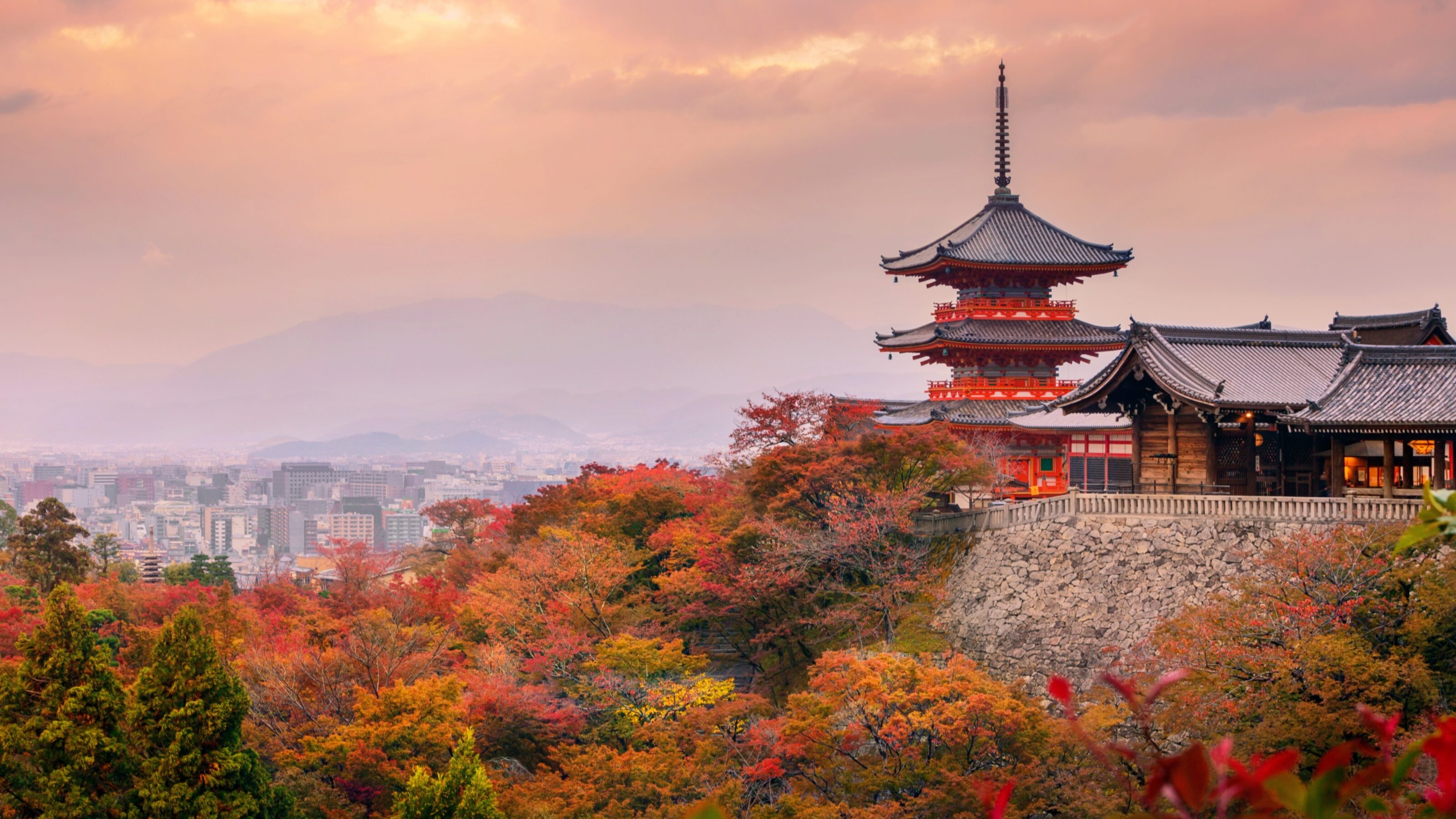 Multi-story pagoda rising above vibrant red and orange autumn trees under a hazy sunset sky.