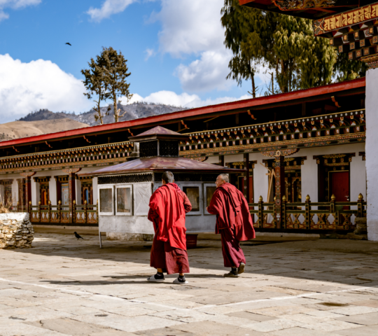 Monks in traditional robes walking in front of a Bhutanese monastery