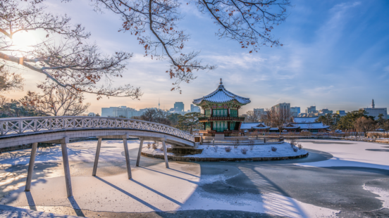 The Hyangwonjeong Pavilion and bridge in Gyeongbokgung Palace grounds are surrounded by a snowy and frozen pond in winter.