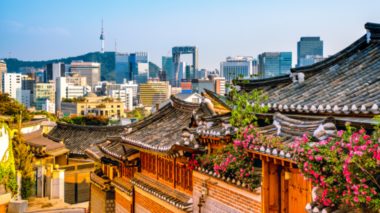 Traditional Korean hanok roofs in the foreground overlook the modern skyline of Seoul with the N Seoul Tower visible.