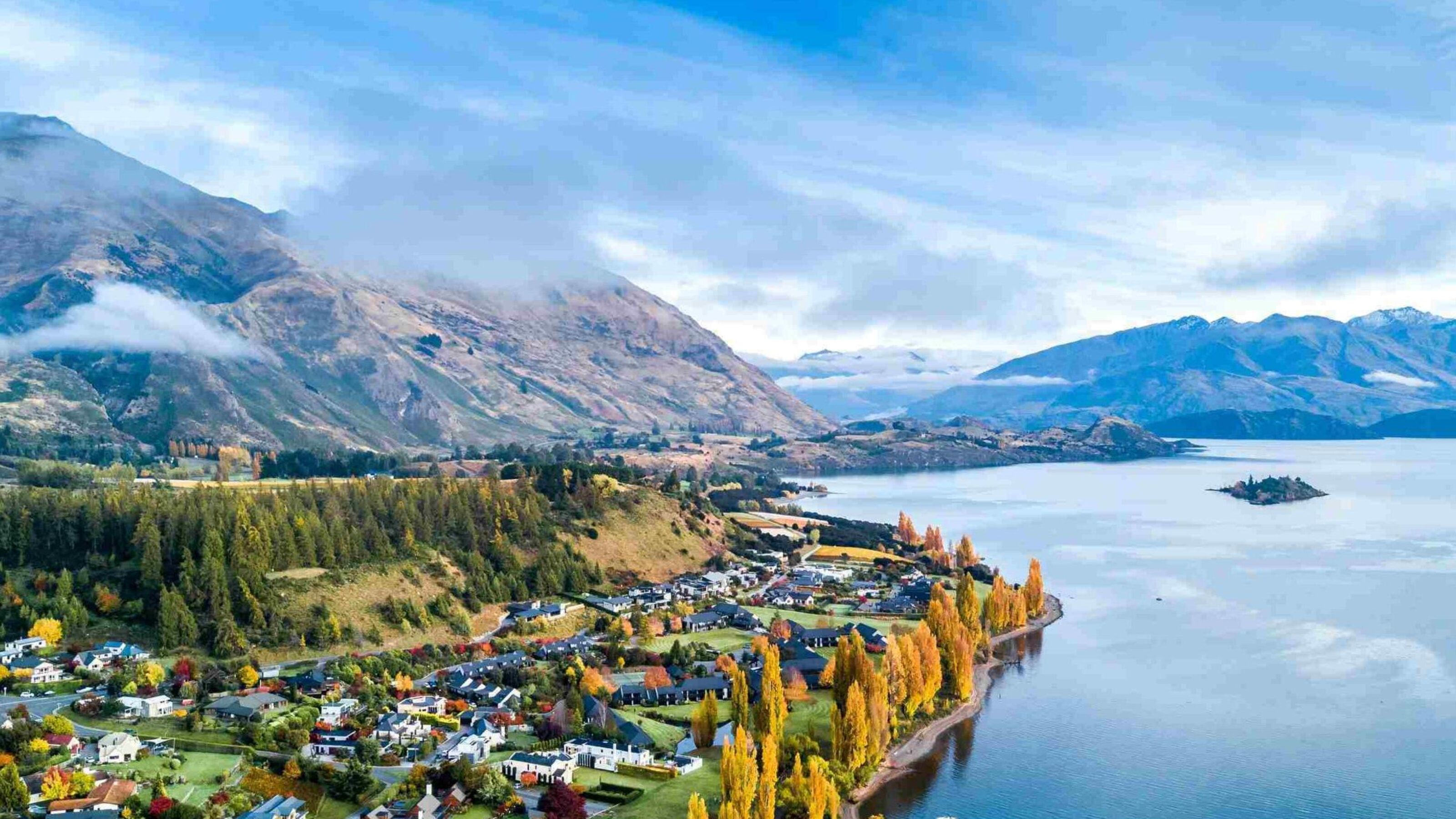 Small town surrounded by yellow autumn trees on a shore of pristine lake with mountains on the background. Wanaka, Otago, South Island, New Zealand