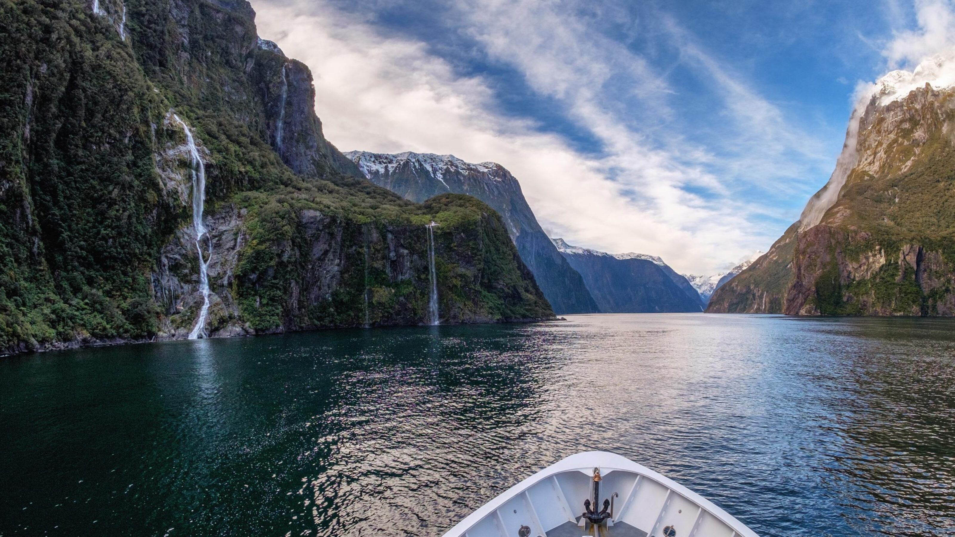 The prow of a boat cruises past waterfalls along Milford Sound, New Zealand