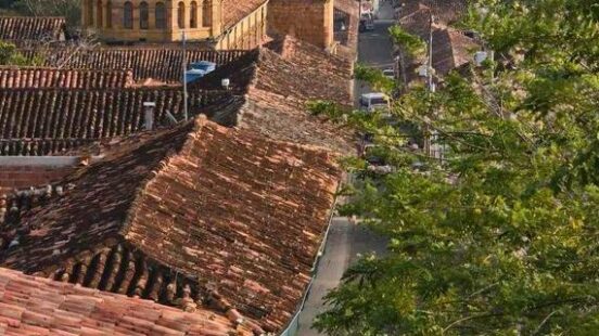 A colonial street in Colombia with red-tiled roofs leading toward a large stone church dome.