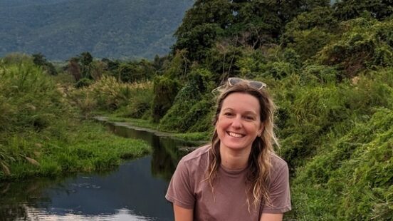 Person sitting on a boat with a backdrop of mountains and lush greenery.