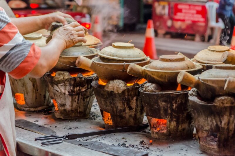 Steam rises from several clay pots cooking over hot coals during luxury Malaysia tours.