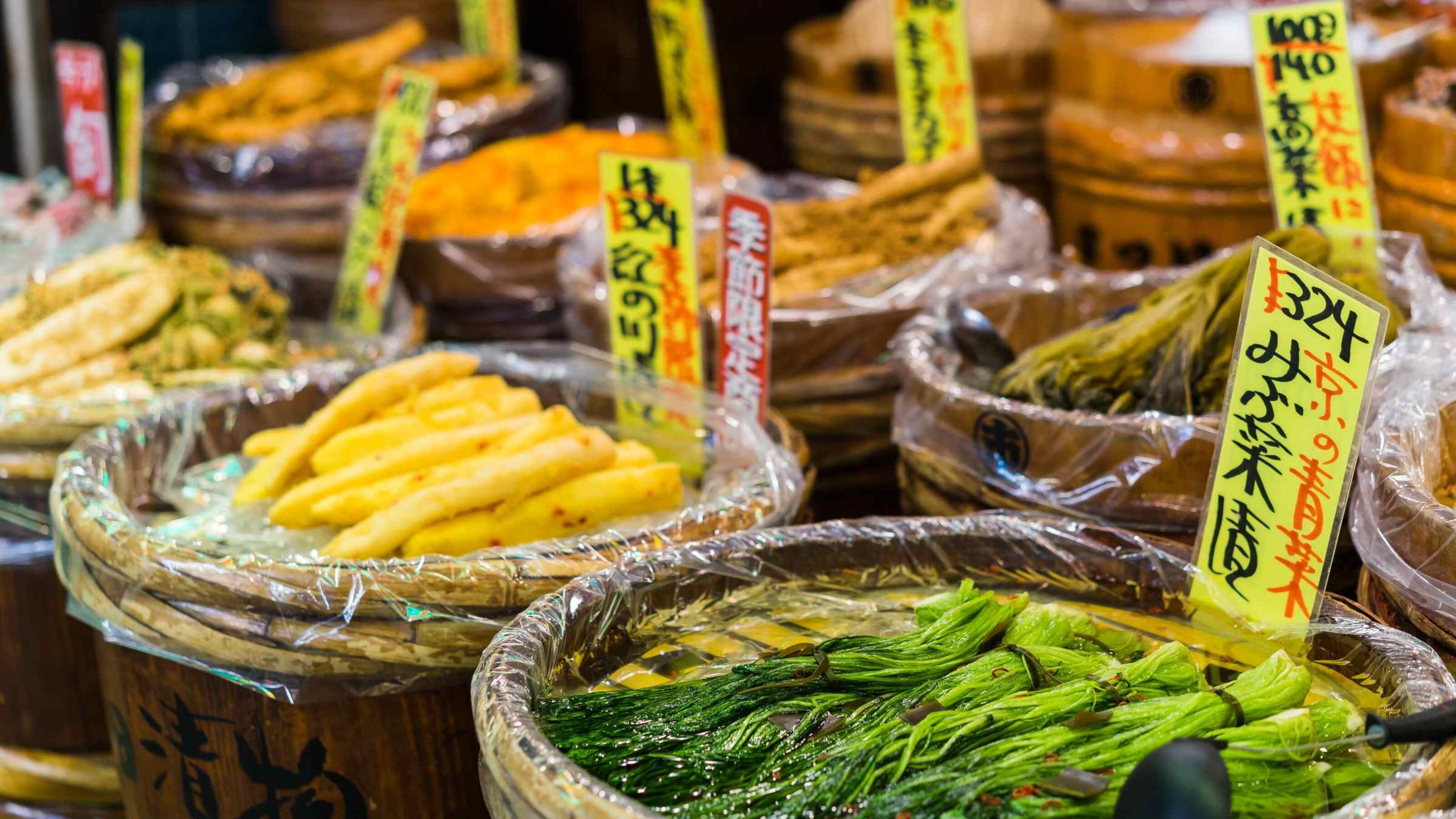 Assorted pickled vegetables displayed in baskets with price tags at a market.