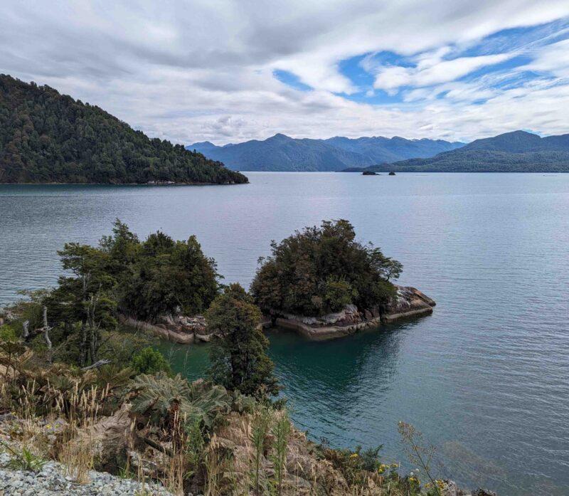Scenic view of a tranquil blue lake with small green islands and mountainous backdrop.