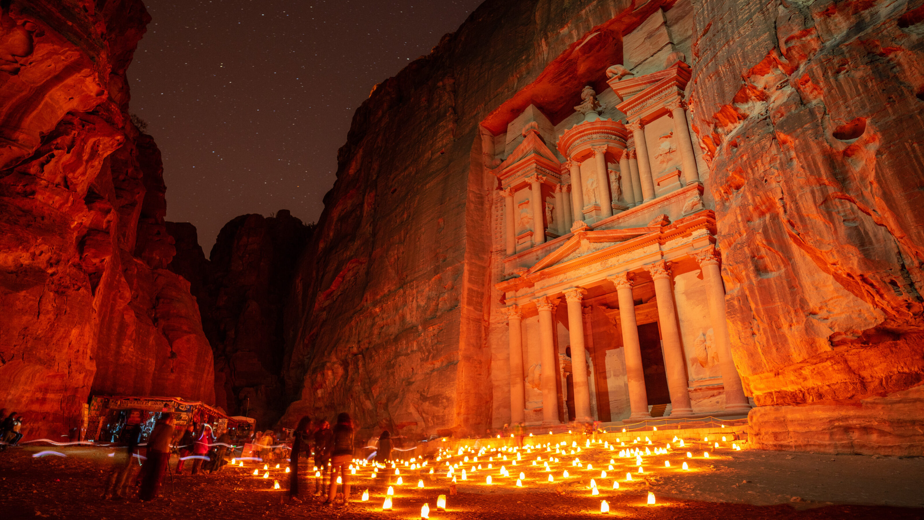 Night view of Al-Khazneh in Petra with candles and starry sky.