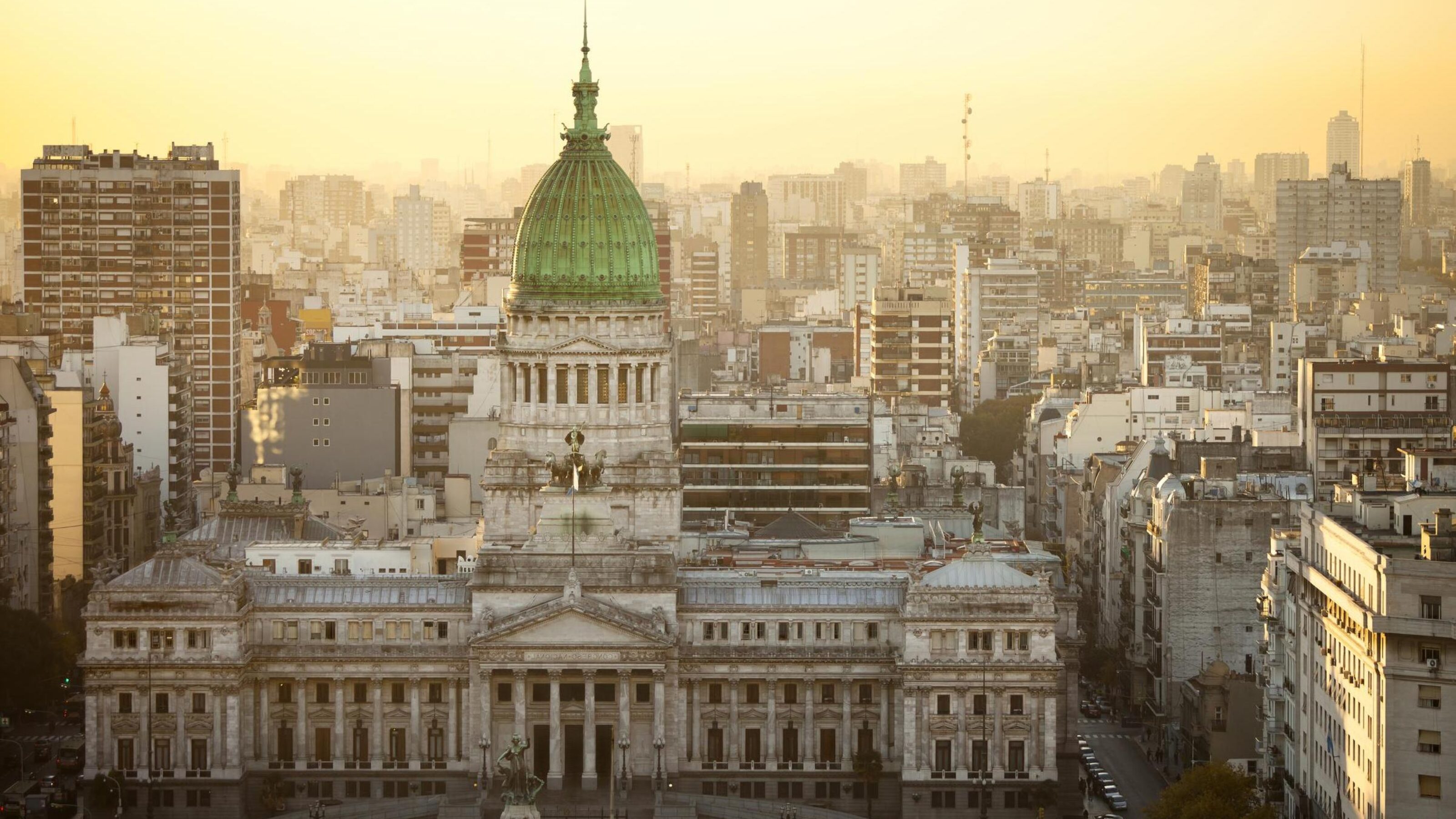 Sunset view of a grand domed building amidst a densely packed cityscape.