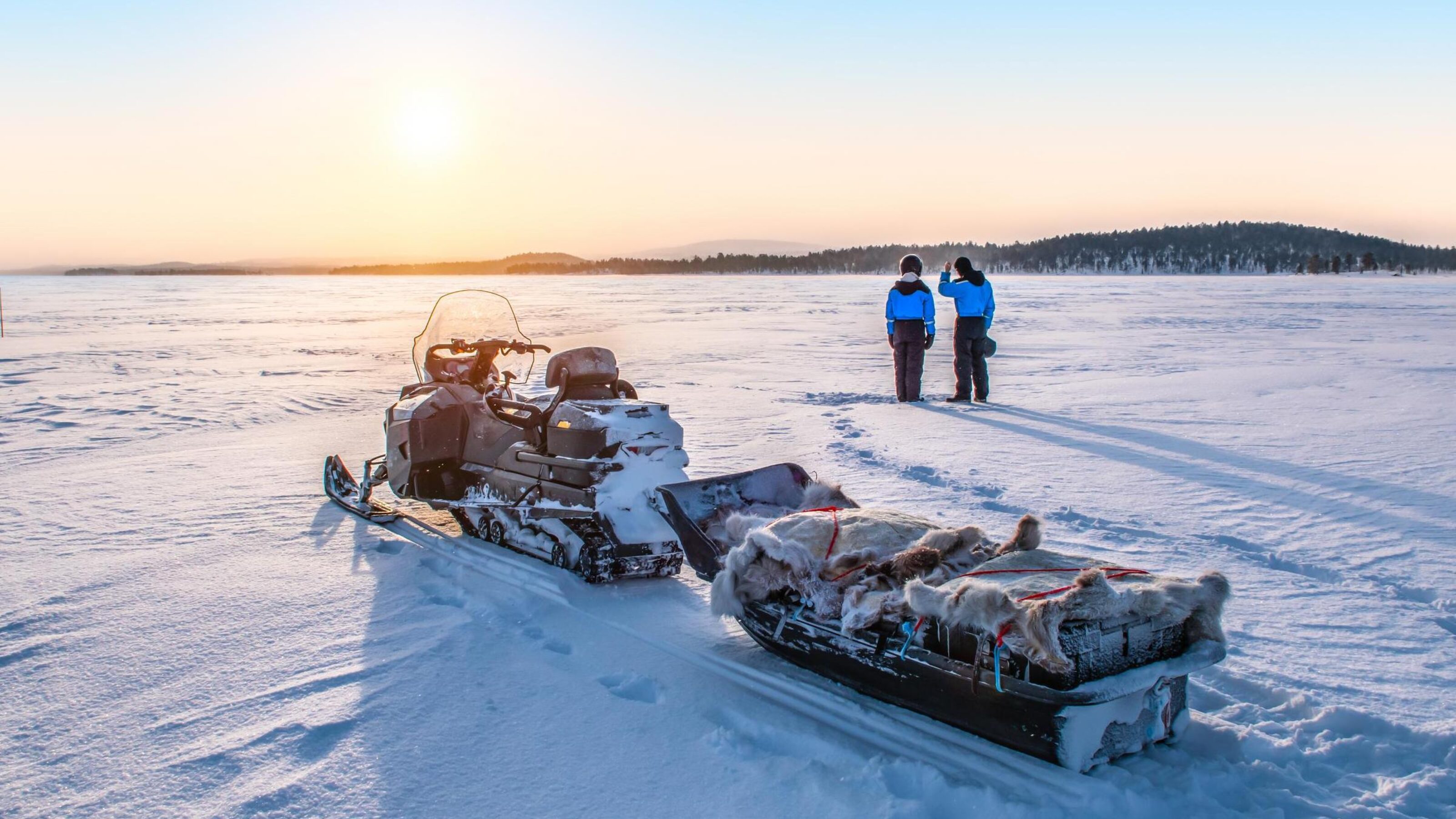 Two people watching sunset with a snowmobile in Finnish Lapland